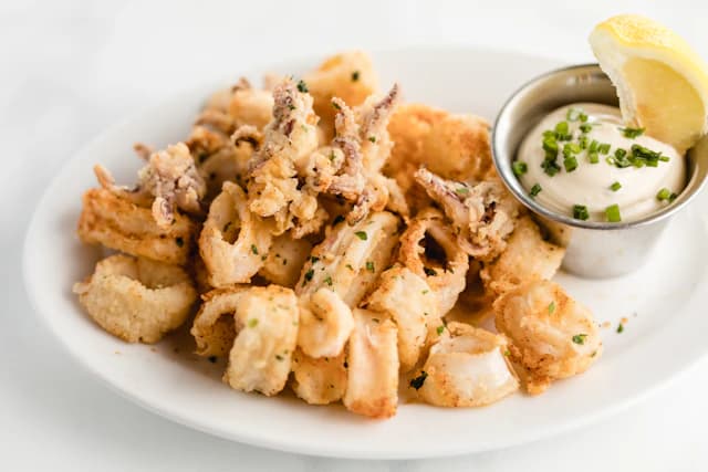 Golden fried calamari rings with lemon and dipping sauce — illustrative stock photograph