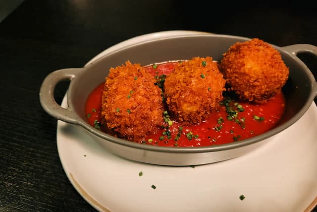 Golden crumbed arancini in tomato sauce — illustrative stock photograph