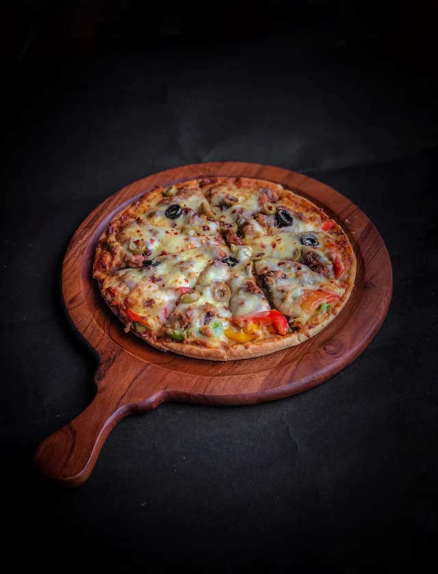 Pizza topped with mushrooms, peppers and olives on a wooden board — illustrative stock photograph
