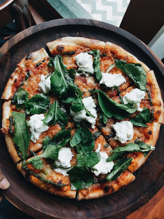 Pizza with green leaves, pesto and dollops of white cheese — illustrative stock photograph