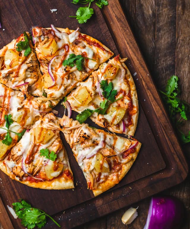 Sliced chicken pizza with pineapple, red onion and herbs — illustrative stock photograph