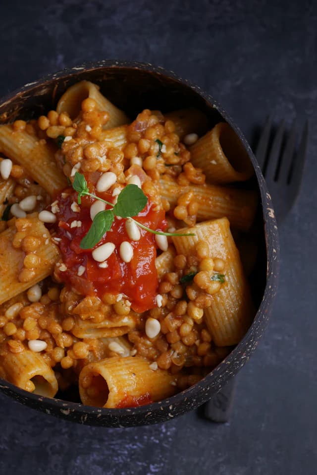 Rigatoni pasta with tomato, lentils and pine nuts in a dark bowl — illustrative stock photograph
