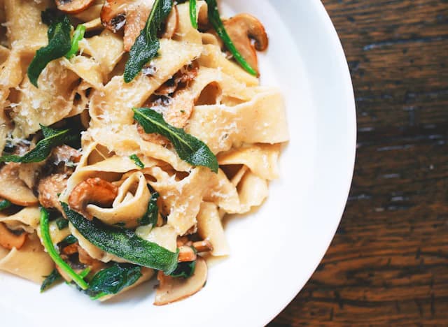 Broad pappardelle ribbons with mushrooms, greens and grated cheese — illustrative stock photograph