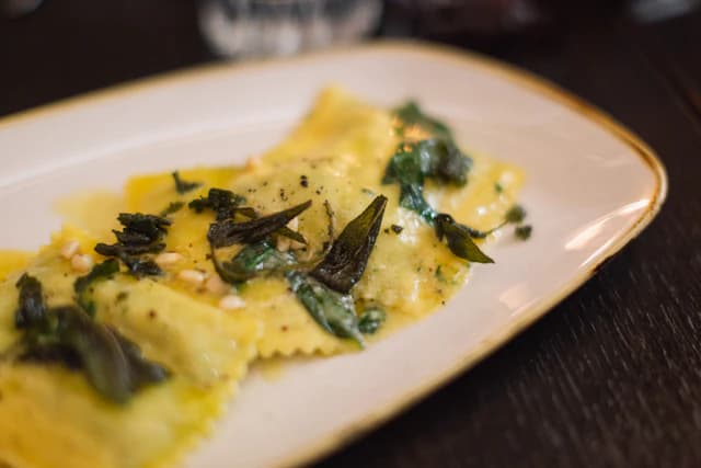 Filled ravioli with grated cheese and green herbs on a white plate — illustrative stock photograph