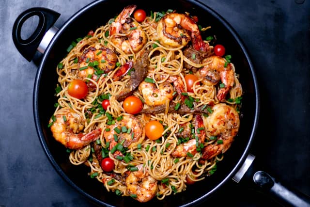 Shrimp and long pasta with tomatoes and chopped green herbs — illustrative stock photograph