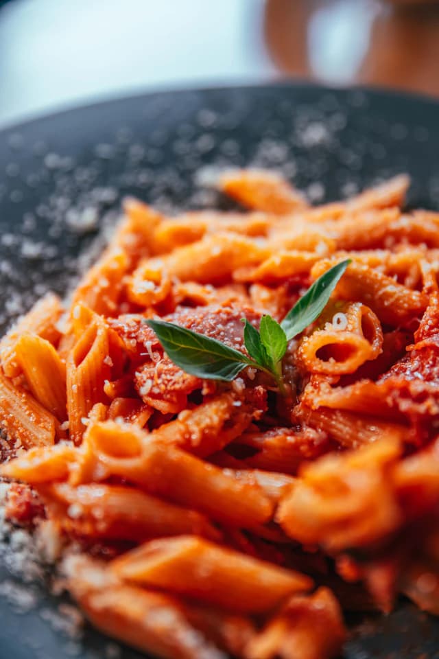 Penne pasta in tomato sauce with a fresh basil sprig — illustrative stock photograph