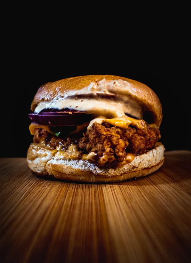 Crispy chicken burger with red onion and creamy sauce — illustrative stock photograph