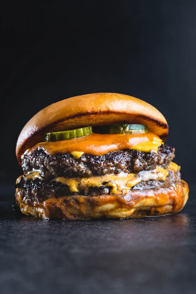 Stacked double cheeseburger on a dark background — illustrative stock photograph