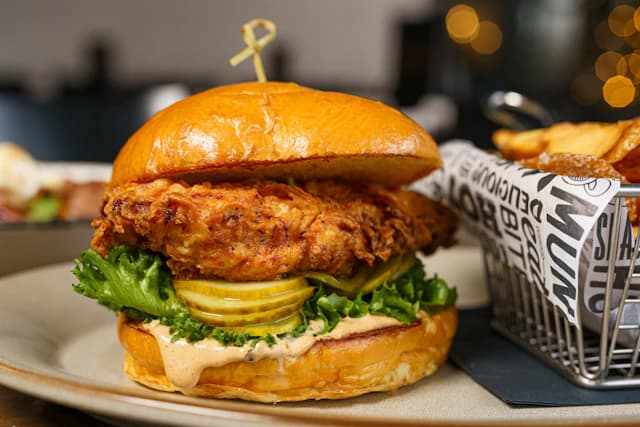 Crispy chicken sandwich with lettuce and pickles beside fries — illustrative stock photograph