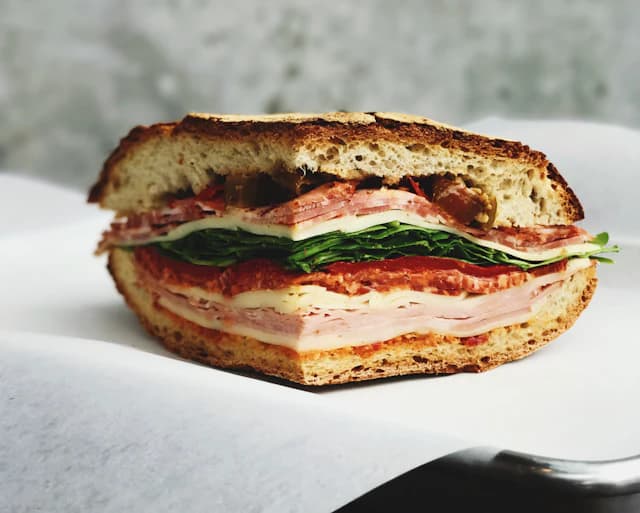 Focaccia sandwich layered with tomato, cheese and green leaves — illustrative stock photograph