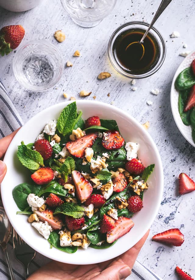 Leafy salad topped with sliced strawberries and nuts — illustrative stock photograph