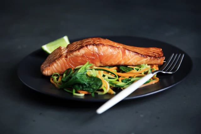 Cooked salmon fillet with green vegetables on a dark plate — illustrative stock photograph