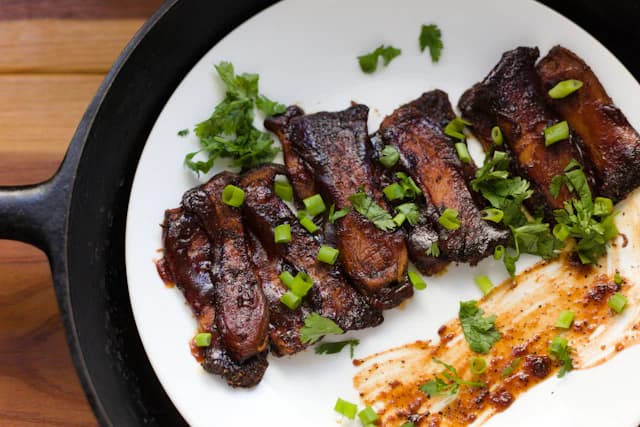 Glazed beef ribs garnished with chopped green herbs — illustrative stock photograph