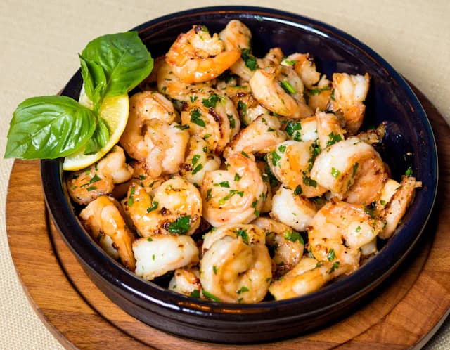 Cooked shrimp with garlic and herbs in a dark bowl — illustrative stock photograph