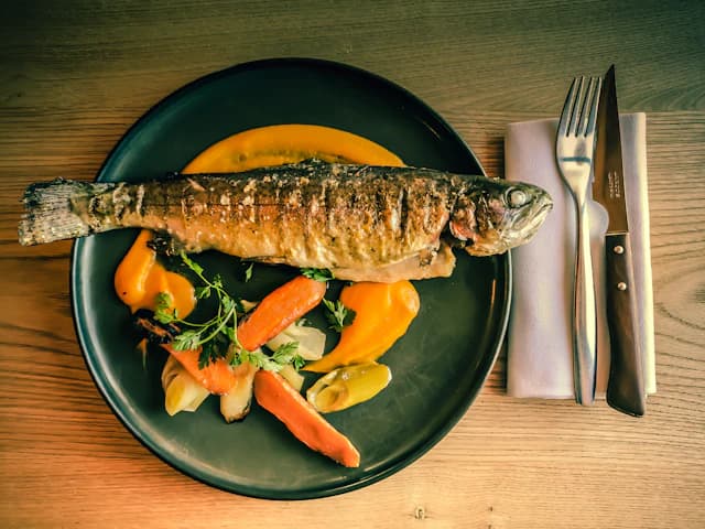 Cooked whole trout served with vegetables on a green plate — illustrative stock photograph