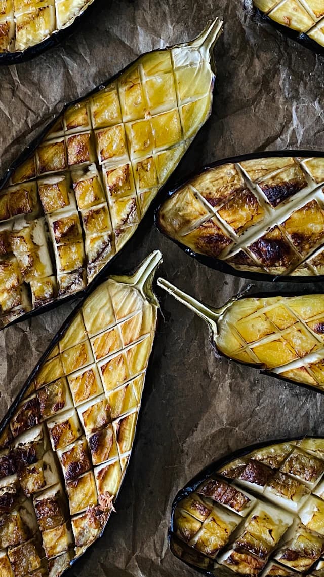 Crosshatched roasted aubergine halves on baking paper — illustrative stock photograph