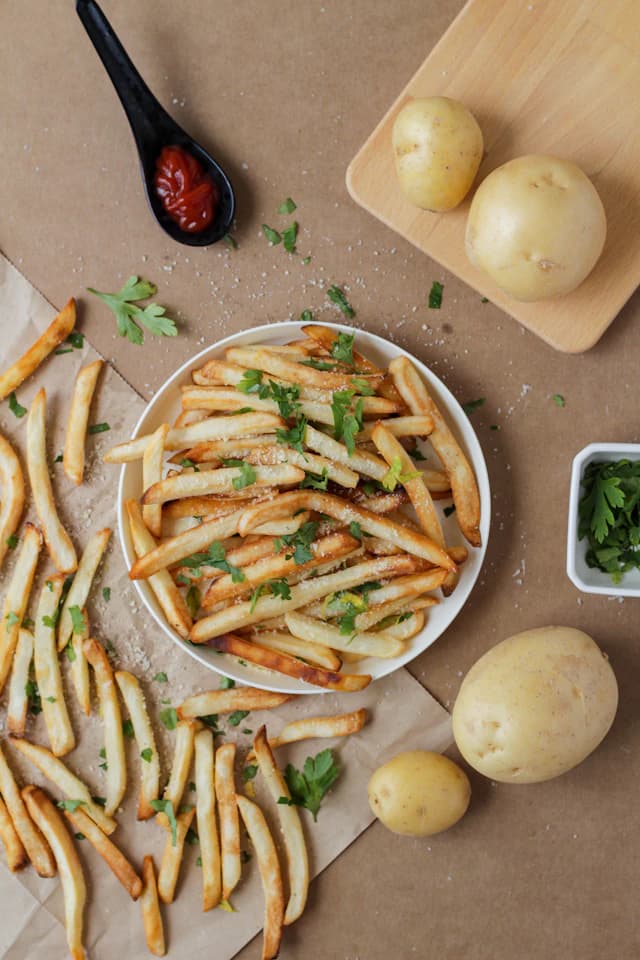 Fries scattered with grated cheese and green herbs — illustrative stock photograph