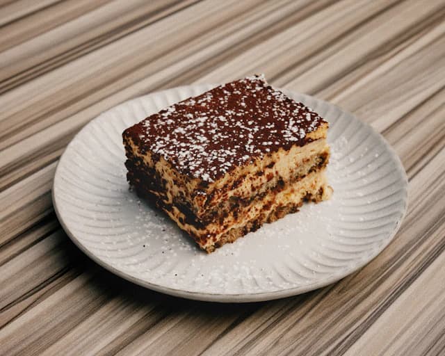 Slice of cocoa-dusted tiramisu on a white plate — illustrative stock photograph