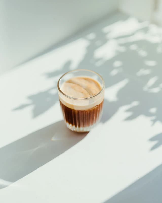 Glass of latte coffee on a sunlit table — illustrative stock photograph
